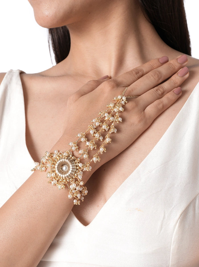 Aadhira Pearl Bridal Haathphool handcrafted with faux pearls, glass bead clusters, and brass metal in a Gold Tone Finish, featuring a floral centerpiece with cascading pearl strands, adjustable finger ring, and bracelet design, perfect for weddings, mehendi, haldi, receptions, and bridal styling.