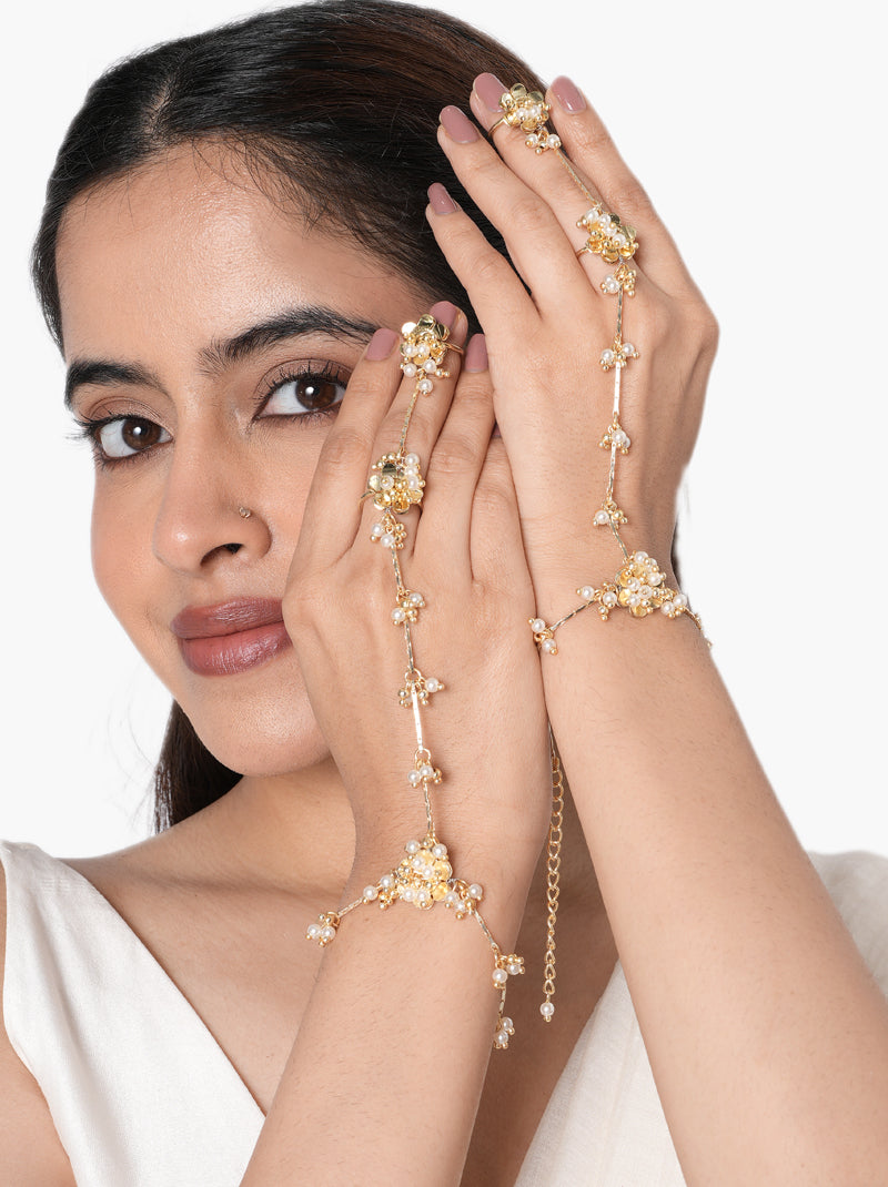 Adhika Delicate Pearl Hathphool pair handcrafted with floral faux pearl motifs, intricate glass bead detailing, elegant hand chains, and a Gold Tone Finish, perfect for Haldi, Mehndi, weddings, receptions, engagement ceremonies, destination weddings, and sophisticated bridal hand styling.
