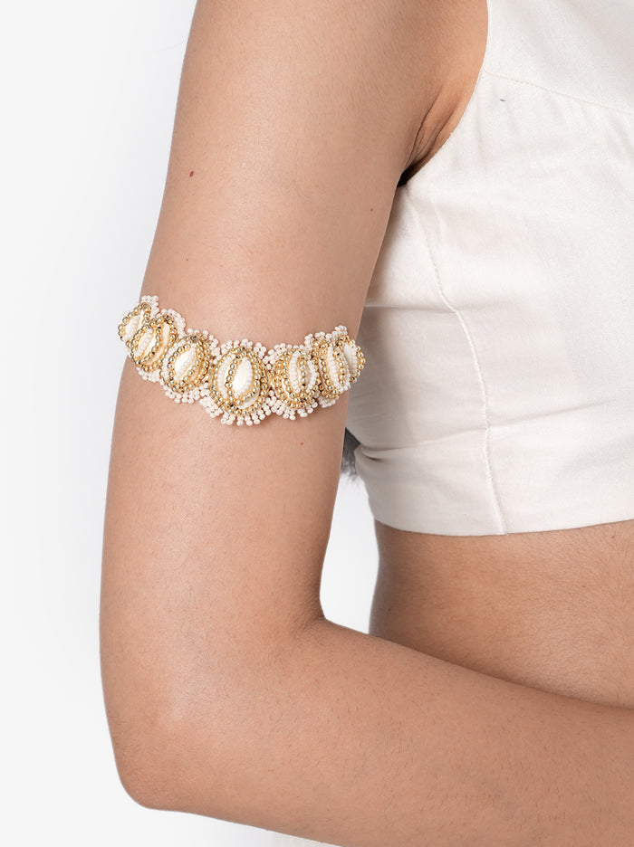 Lorena Embroidered Shell Bajuband handcrafted with natural cowrie shells, faux pearls, intricate glass bead embroidery, thread detailing, a stretch beaded band, and a Gold Tone Finish, perfect for Haldi, Mehndi, weddings, receptions, destination weddings, and elegant bridal arm styling.