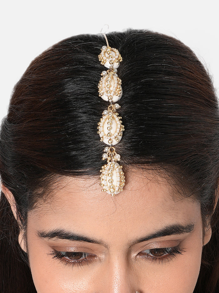 Ritika Shell Ethnic Maangtika handcrafted with vertically arranged natural cowrie shells, faux pearls, intricate glass bead detailing, and a Gold Tone Finish, perfect for Haldi, Mehndi, weddings, festive celebrations, poojas, and elegant bridal styling.
